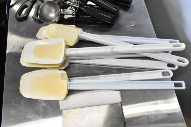 Lot of kitchen utensils including scrapers and dishers, various sizes, used condition, with visible wear on spatulas.