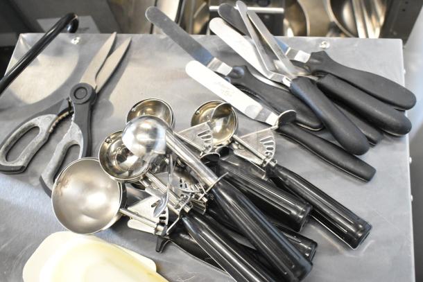 Lot of kitchen utensils including dishers, scrapers, and scissors. Features black handles, stainless steel material.