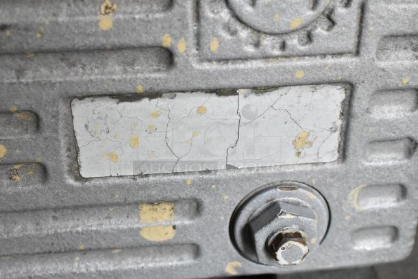 Rustic metal motor casing with visibly cracked and worn label. Features textured surface and large bolt, indicating older condition.