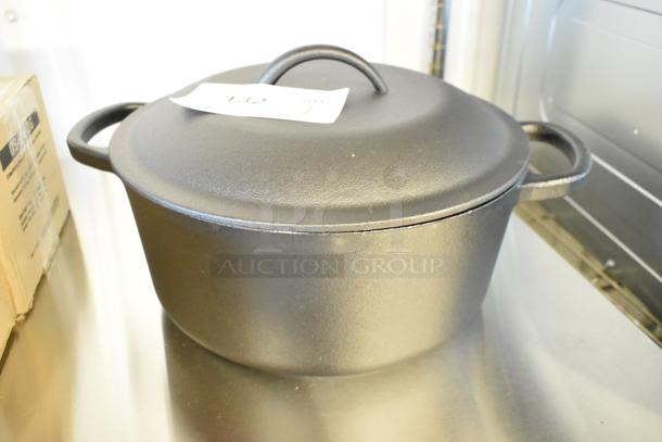Brand new cast iron Dutch oven, scratch and dent condition, with flat lid and handles. Auction tag visible.