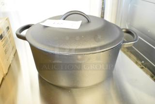 Brand new cast iron Dutch oven, scratch and dent condition, with flat lid and handles. Auction tag visible.