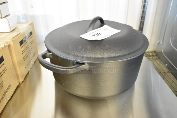 Brand new cast iron Dutch oven with minor scratches and dents. Black finish, round shape, side handles, and lid tag visible.