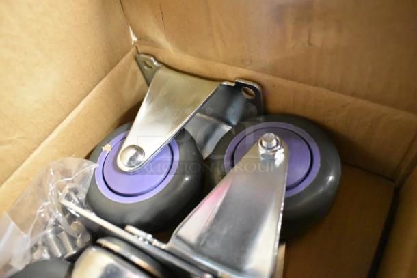 Lot of 4 brand new commercial casters, scratch and dent condition, purple wheels, metal brackets, in a cardboard box.