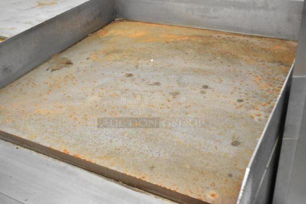 Stainless steel commercial countertop gas flat top griddle, showing wear with grease stains on the surface.