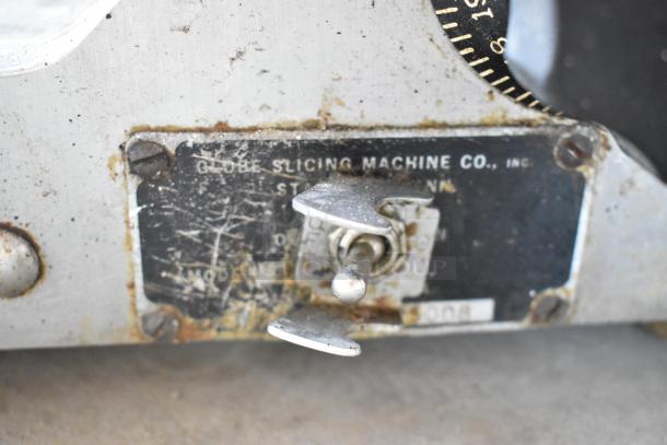 Globe stainless steel commercial countertop meat slicer with a blade sharpener, visible rust and wear, labeled "Globe Slicing Machine Co., Inc."
