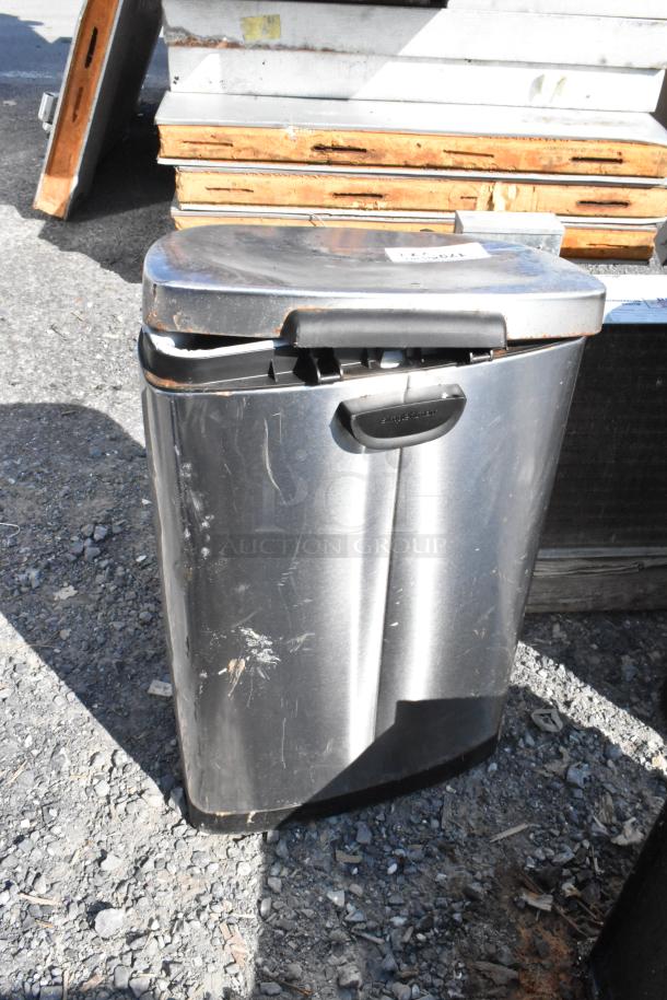 Two metal trash cans, one visible, in worn condition. Stainless steel with scratches and dents. Black plastic lid and handle.