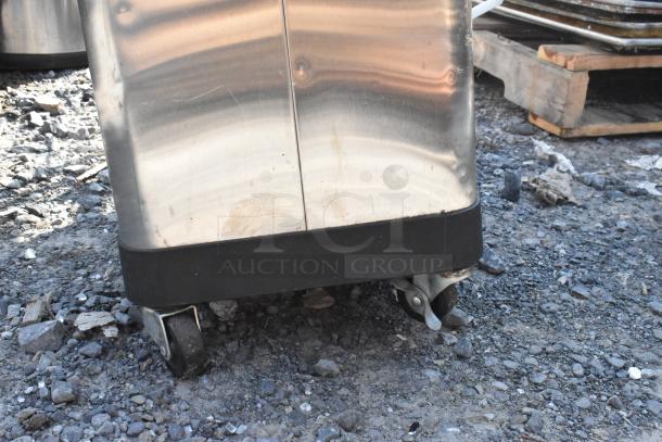 Two metal trash cans on wheels, showing signs of wear, resting on a gravel surface.