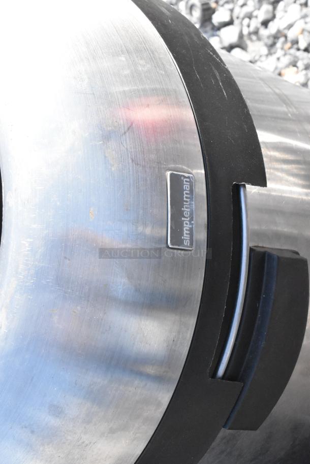 Two metal trash cans, one visible labeled "simplehuman," stainless steel with black trim, in outdoor setting.