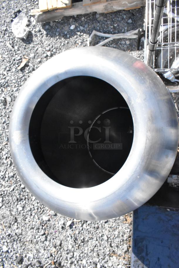 Two metal trash cans, cylindrical with wide openings, in used condition on gravel surface.