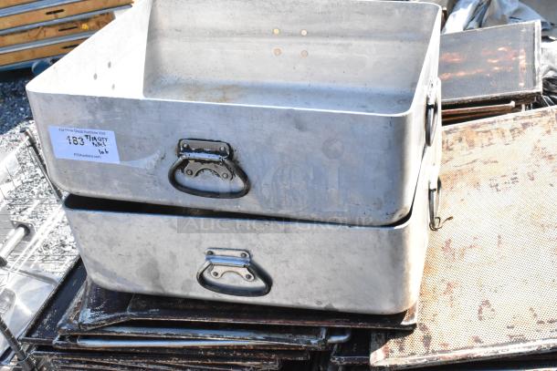 Metal roasting pans and perforated baking sheets in used condition, stacked outdoors. Auction tag visible.