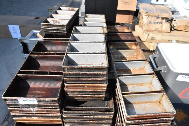 Lot of metal 4-loaf baking pans, various conditions, stacked outdoors with visible rust and wear.