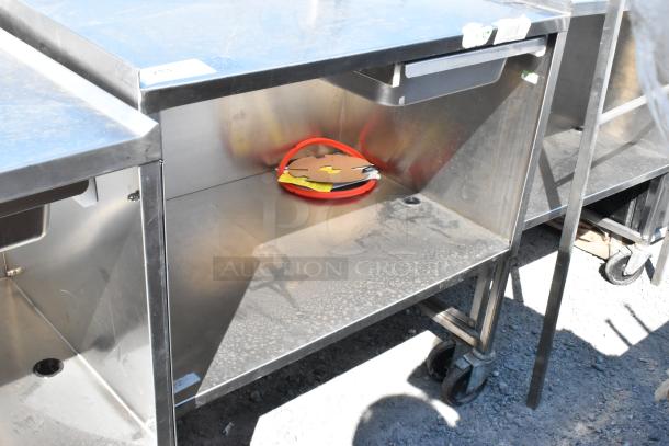 Stainless steel cart with under shelf, commercial casters, visible wear, includes a coiled hose.