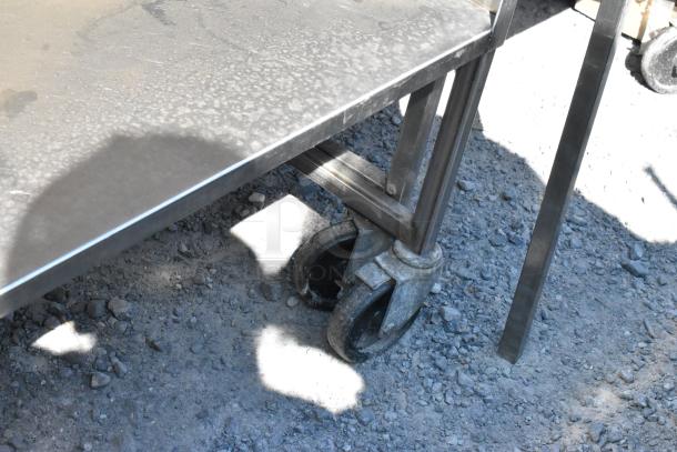 Stainless steel cart with under shelf on commercial casters, visible wear, ideal for industrial use.