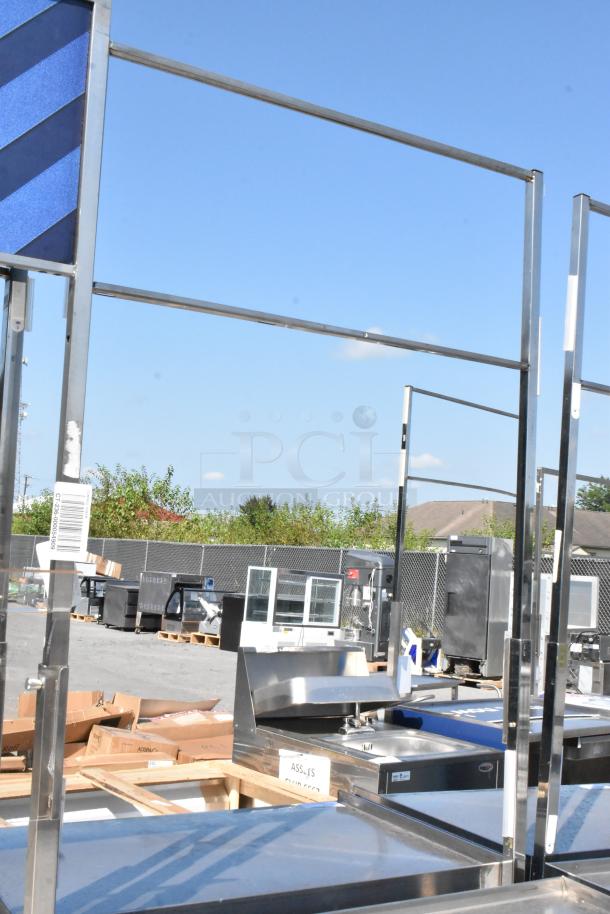 Stainless steel cart with under shelf on commercial casters, barcode tag visible, outdoor setting.