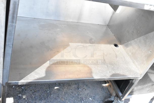 Stainless steel cart with under shelf, commercial casters. Minor surface wear, sturdy design for industrial use. Suitable for storage and transport.