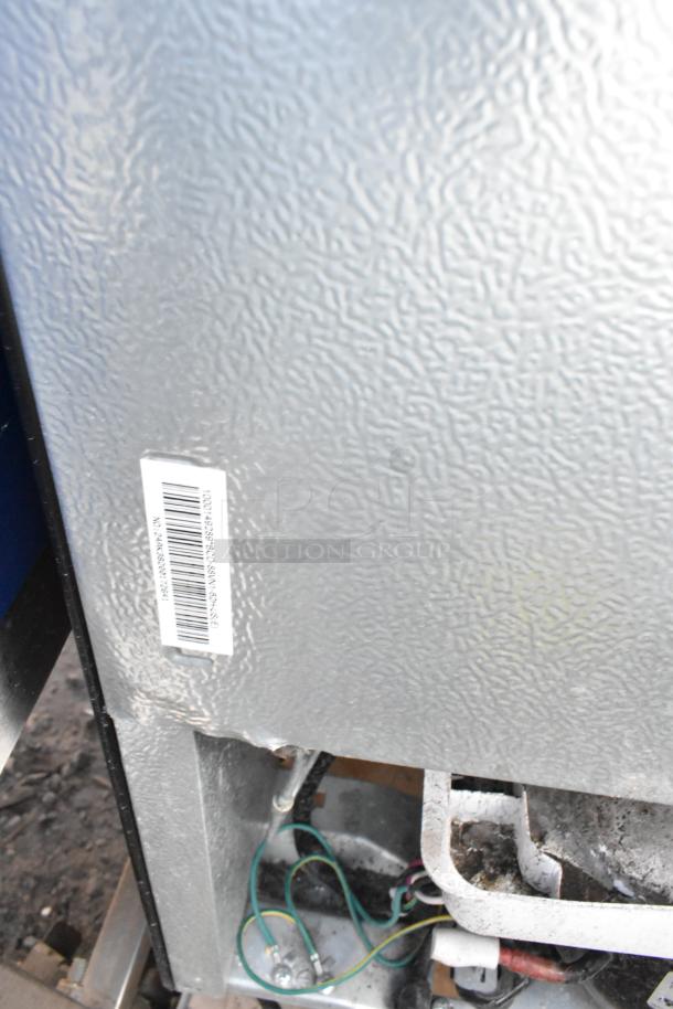 Close-up of a textured metal surface with a barcode label. Background shows wiring and mechanical parts.