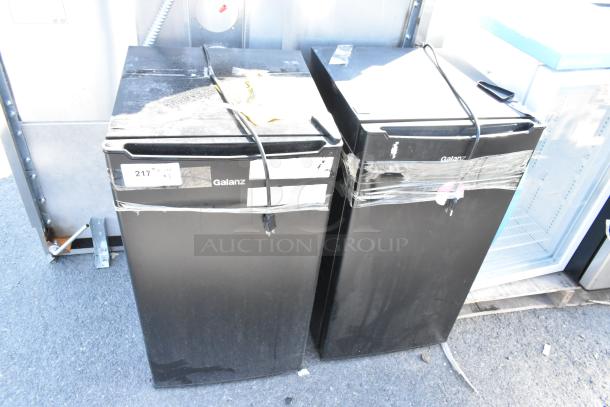 Two Galanz GLR33MBKE23 mini coolers, black, 120 volts, 1 phase, taped cords, visible wear. Auction includes both units.