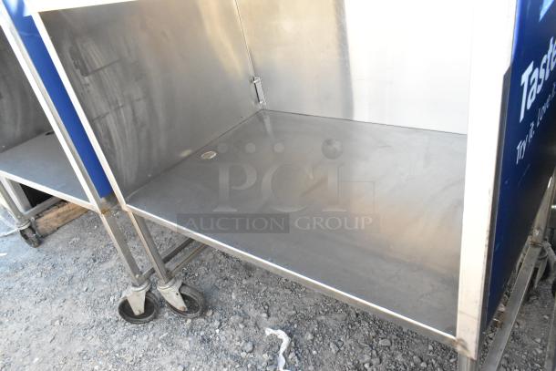 Stainless steel cart with under shelf, mounted on commercial casters. Slight wear visible on metal surfaces.