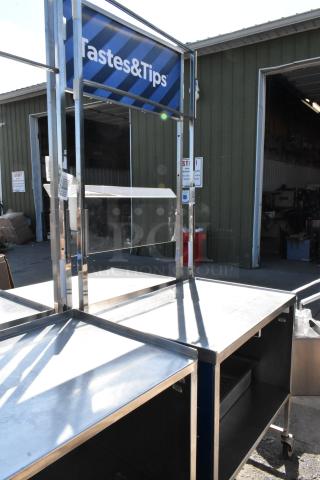 Stainless steel cart with under shelf, on commercial casters. Features sturdy design, used condition, and "Tastes & Tips" signage.