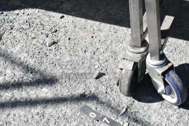 Stainless steel cart with under shelf, featuring commercial casters. Shown on textured surface; partial view of wheels.