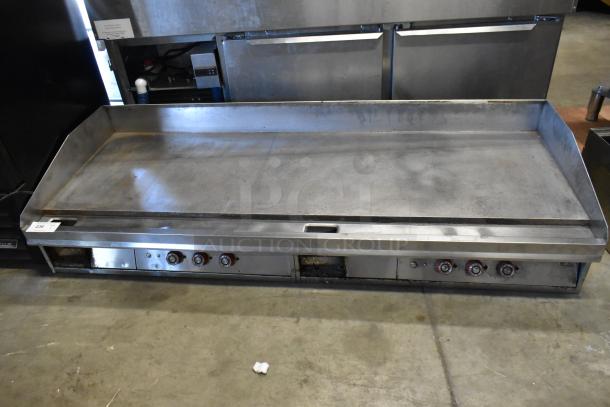 Stainless steel commercial countertop griddle with thermostatic controls, four knobs, and flat top, showing signs of use.