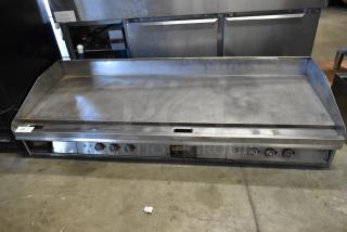 Stainless steel commercial countertop griddle with thermostatic controls, four knobs, and flat top, showing signs of use.
