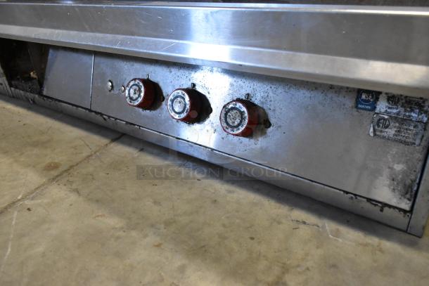 Stainless steel commercial countertop flat top griddle with three thermostatic controls, showing wear, NSF certified.