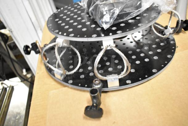 Two-tier unit with perforated black metal plates, secured by metal cables. Appears unused, suitable for organization or display.