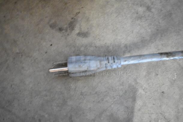 A close-up of a power plug for a 2016 Bizerba GSP H commercial meat slicer, 120V, on concrete surface.