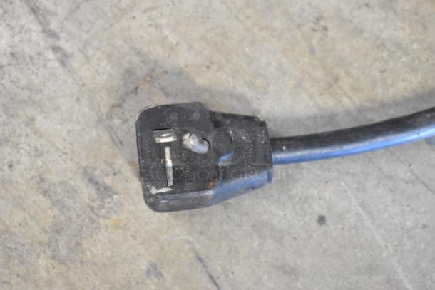 Close-up of power plug for Menumaster MDC182 microwave oven, showing three-prong design and black cord, on concrete floor.