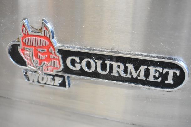 Wolf Gourmet logo on stainless steel commercial gas range with 4 burners, center flat top, and convection oven.