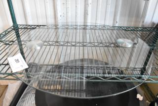 Round glass pane on metal shelf, clear, smooth surface, two circular metal weights on top, auction tag reading "261".