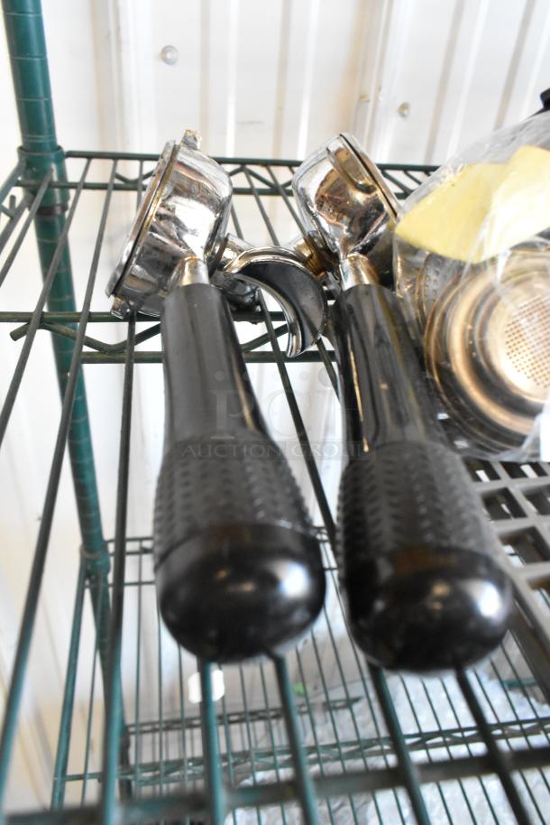 Lot of espresso machine items on a metal rack, including two portafilters with black handles, in used condition.