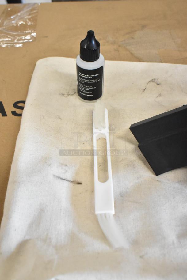 Bottle of lubricant oil and cleaning brush for the Bizerba GSP H meat slicer, placed on a white cloth.