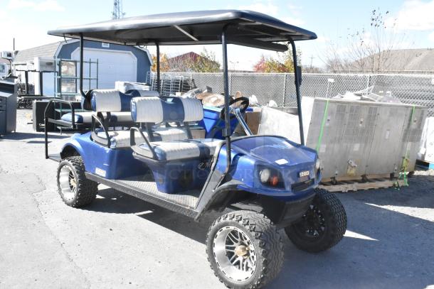 EZ Go blue and white 6-seat golf cart with speaker system. Features off-road tires, canopy roof, and dual-tone seats.