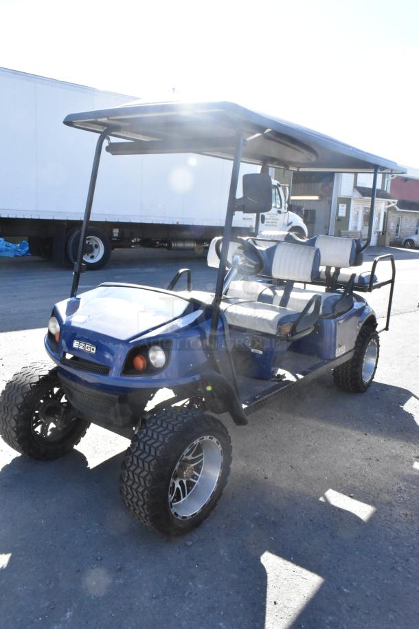 EZ Go blue and white 6-seat golf cart with speaker system, off-road tires, and canopy roof.