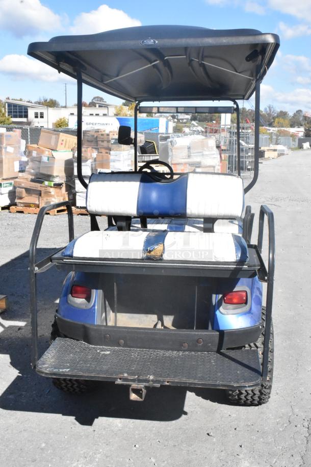 EZ Go blue and white 6-seat golf cart with speaker system, visible wear on seats, sturdy frame, used condition.