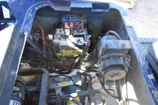 EZ Go golf cart engine compartment with Valucraft battery and wiring. Blue exterior visible, condition indicates use.