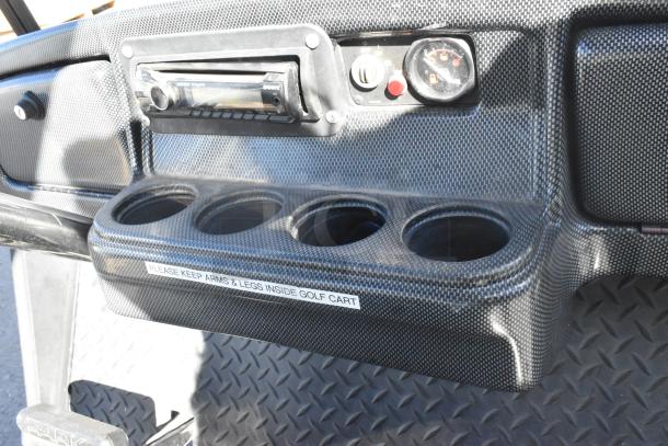 EZ Go golf cart dashboard with carbon fiber styling, featuring a speaker system and four cup holders.