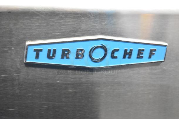 Turbochef HhC2020 logo on stainless steel commercial oven, showing brand name in blue and black lettering.