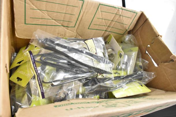 Box of brand new kitchen items, including tongs. Items are individually packaged with yellow tags.