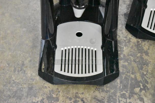 2 Fetco Luxus L3D-15 stainless steel beverage holders with drip trays, black accents, on a textured floor.