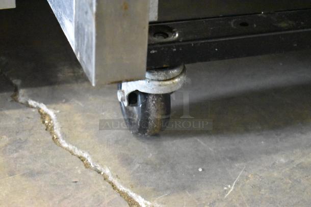 Close-up of a commercial caster on a True T-72 stainless steel reach-in freezer, showing a black wheel and metal frame.