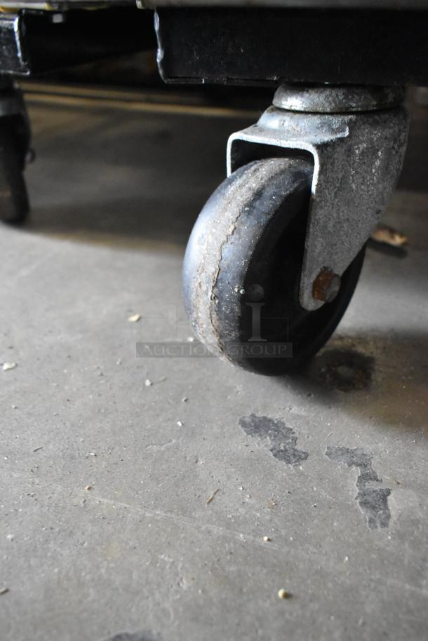 Rusty commercial caster on True T-72 reach-in cooler; metal base attached to black frame, visible wear.