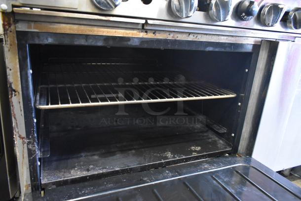 Cookrite stainless steel commercial 4 burner range with flat top griddle, oven, over shelf, and back splash on casters. Visible wear.