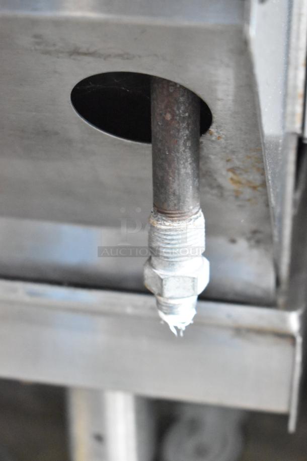 Close-up of stainless steel Bakers Pride CBBQ30S propane gas connection on commercial charbroiler grill. Visible wear on fittings.
