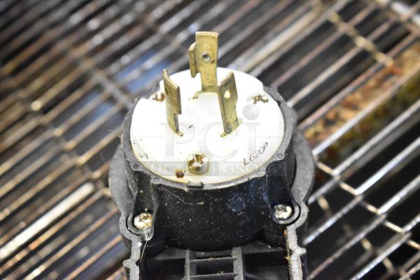 Close-up of an electrical plug component labeled "L620P" on a conveyor pizza oven. Features brass prongs, set against a wire grill background.