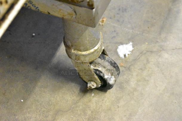 Close-up of a commercial caster on a Middleby Marshall PS638G pizza oven. Slightly worn, on grey concrete floor.