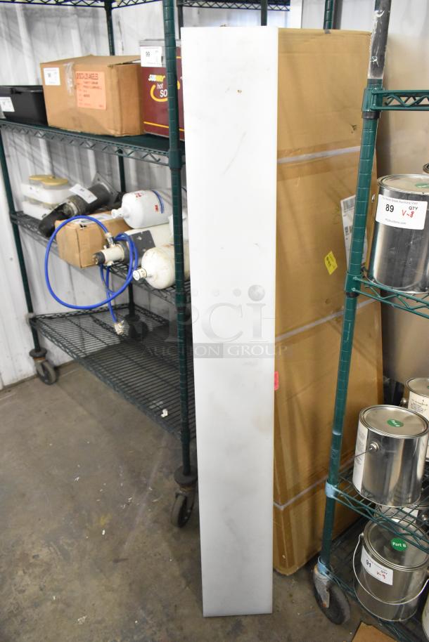 White cutting board, elongated and rectangular, standing upright. Appears slightly worn, suitable for kitchen use.