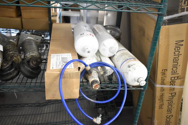Six various water filter cartridges, each labeled with technical details, new condition, bundled with blue connectors on a metal shelf.